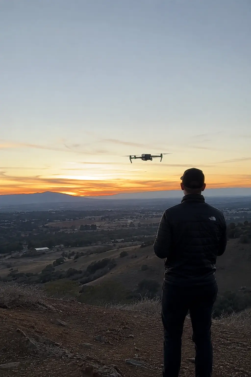 Drone pilot operating a drone at sunset over a scenic valley